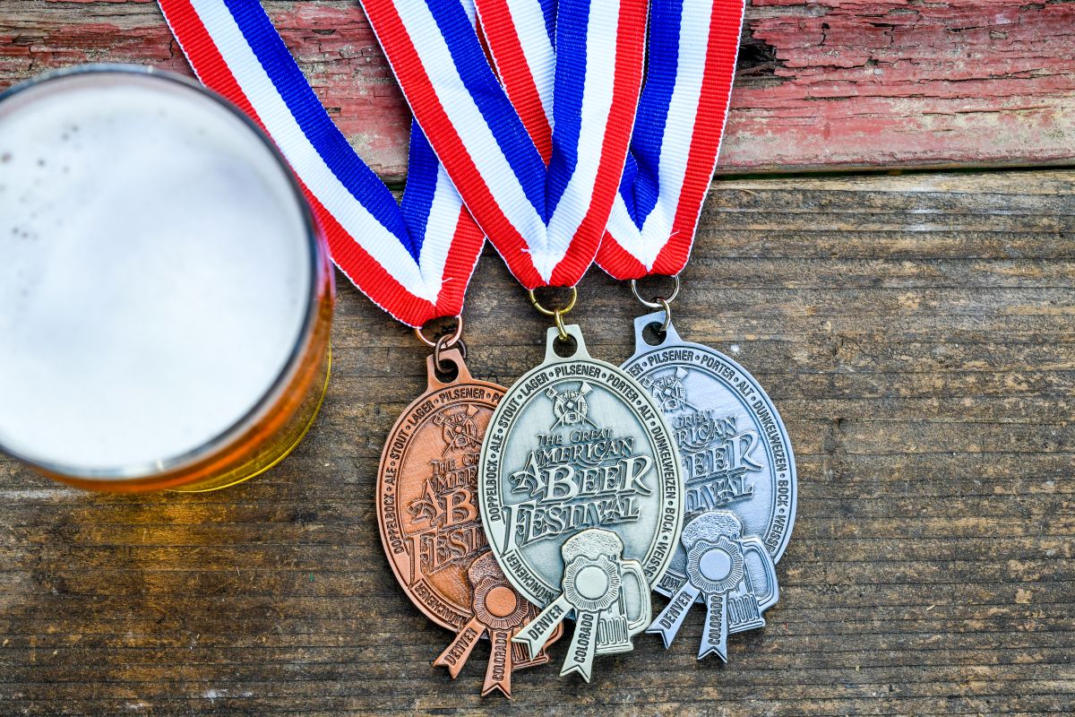 Three Great American Beer Festival medals next to a glass of beer